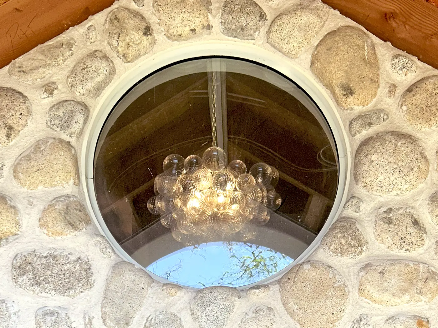 Luxury custom home entry chandelier visible through a round architectural window with professionally installed decorative lighting by Camson Electric.
